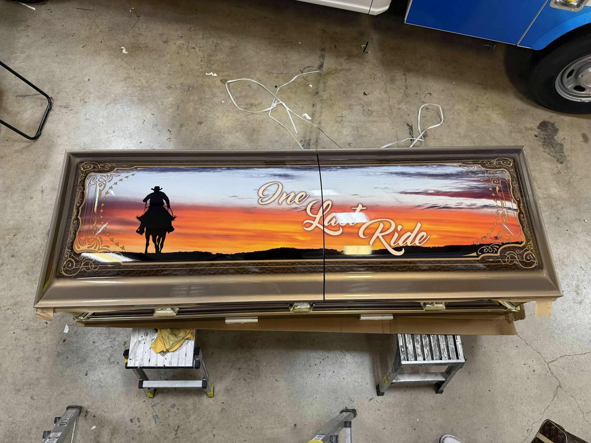 Bronze casket lid wrapped with a cowboy riding at sunset and One Last Ride in cream script
