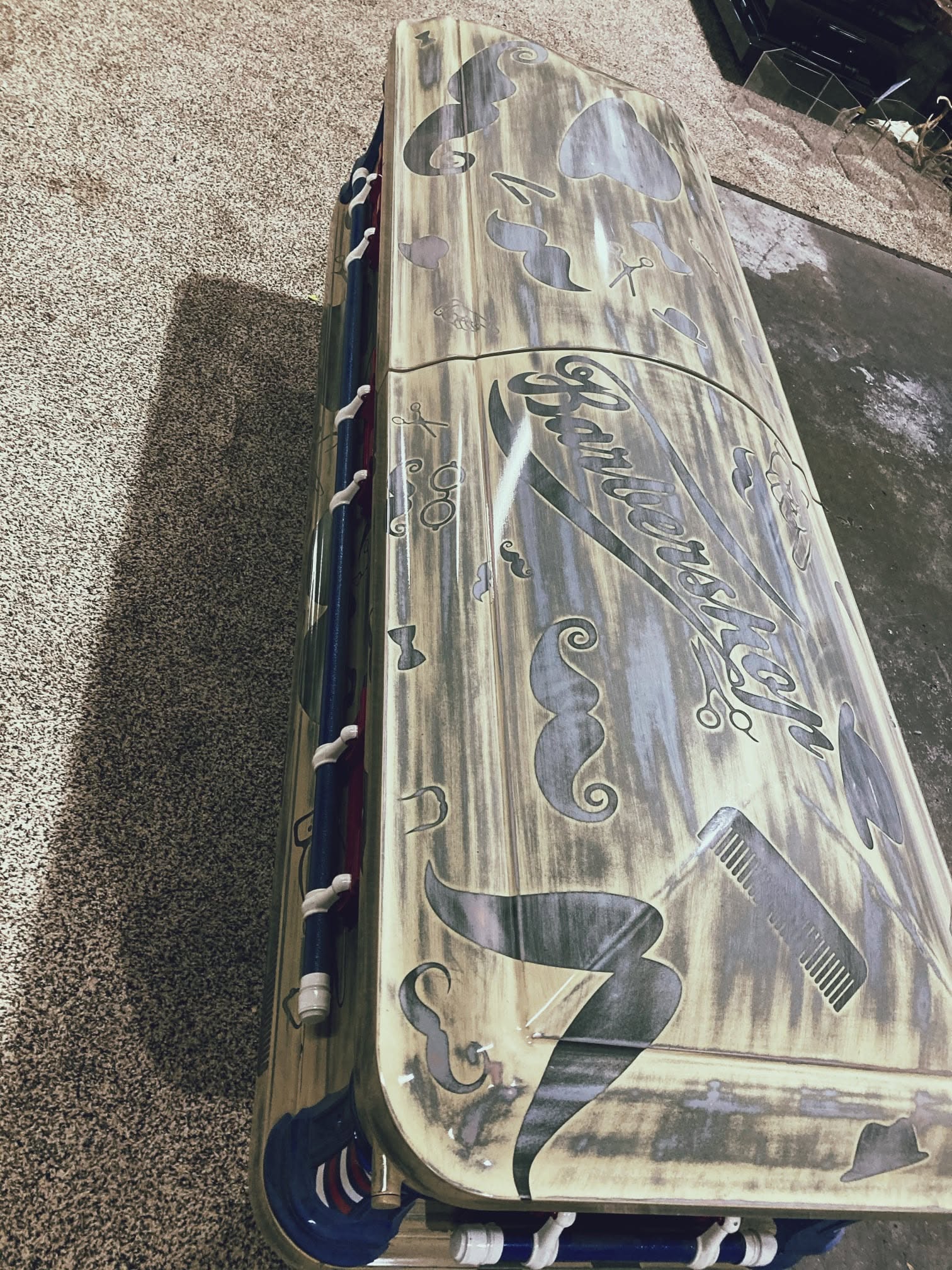Weathered cream casket wrapped with barber poles, combs, mustaches and Barbershop lettering