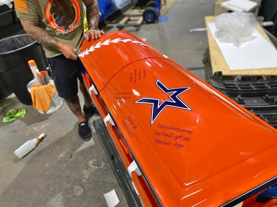 Bright orange casket carrying a navy Astros star and handwritten family messages, still in the shop