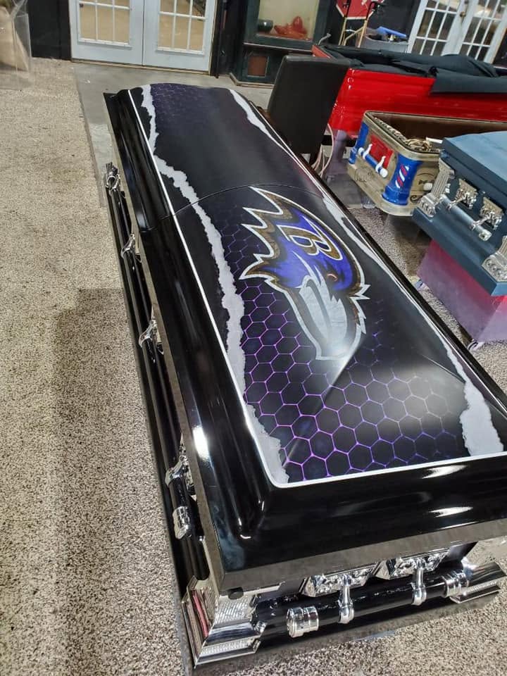 Black casket with a torn metal effect revealing purple honeycomb and a Baltimore Ravens crest