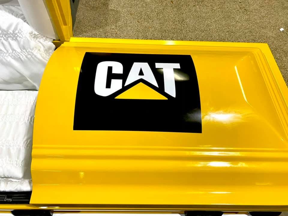 Caterpillar yellow casket with the black and white CAT logo on the lid and white crepe lining