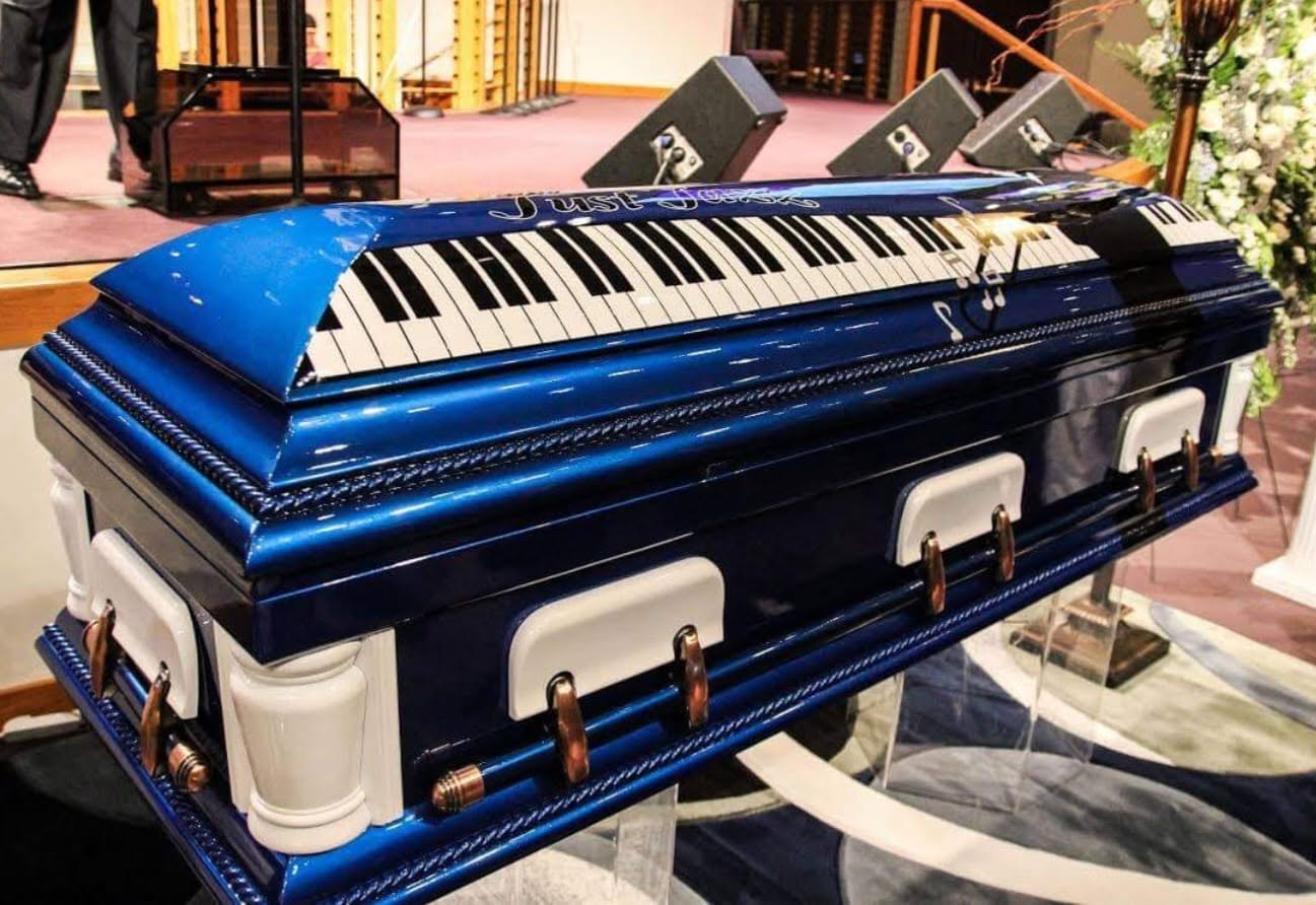 Royal blue casket wrapped with a piano keyboard and Just Jesse in script, set on a church stand