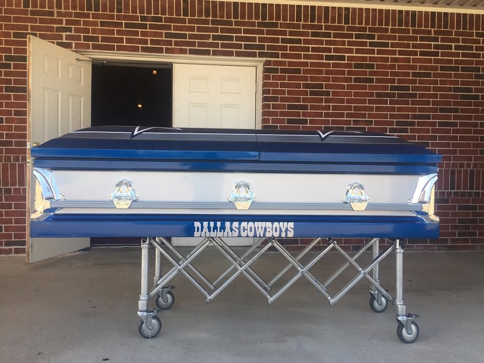 Navy and white casket lettered DALLAS COWBOYS along the base, rolled outside on a church truck
