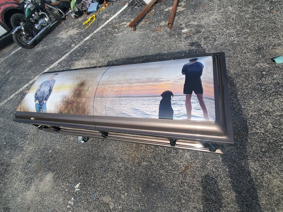 Bronze casket wrapped with a sunrise fishing scene showing a wading angler and his black dog