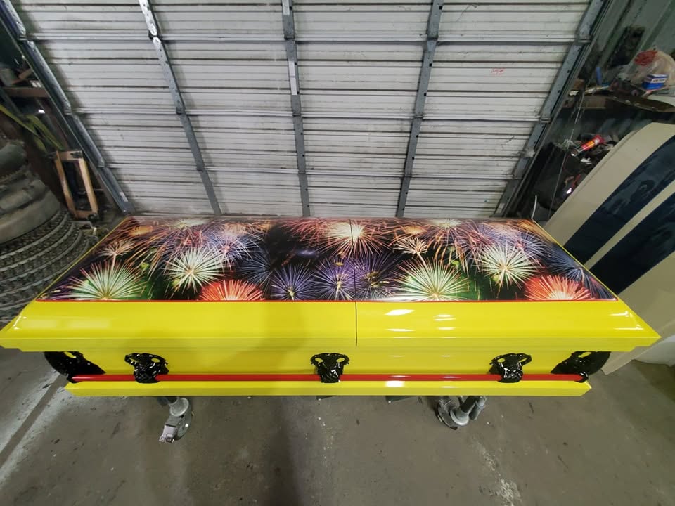 Canary yellow casket crowned with a bursting fireworks mural and red pinstripe over black handles