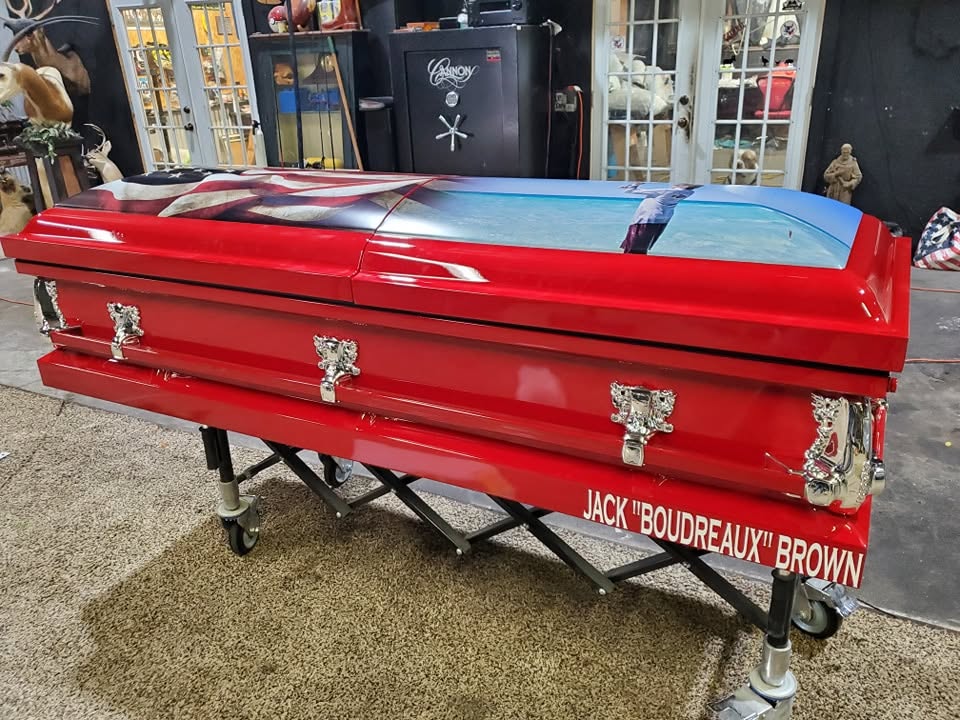 Candy red casket with an American flag and eagle lid mural, lettered Jack Boudreaux Brown