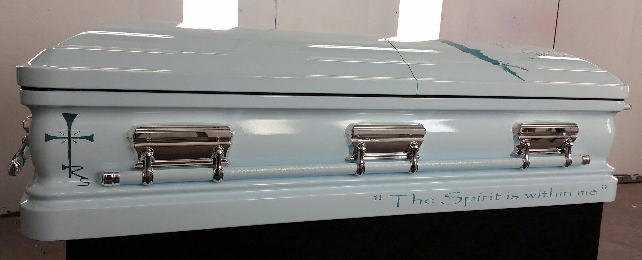 Soft powder blue casket with a slender teal cross and the quote The Spirit is within me