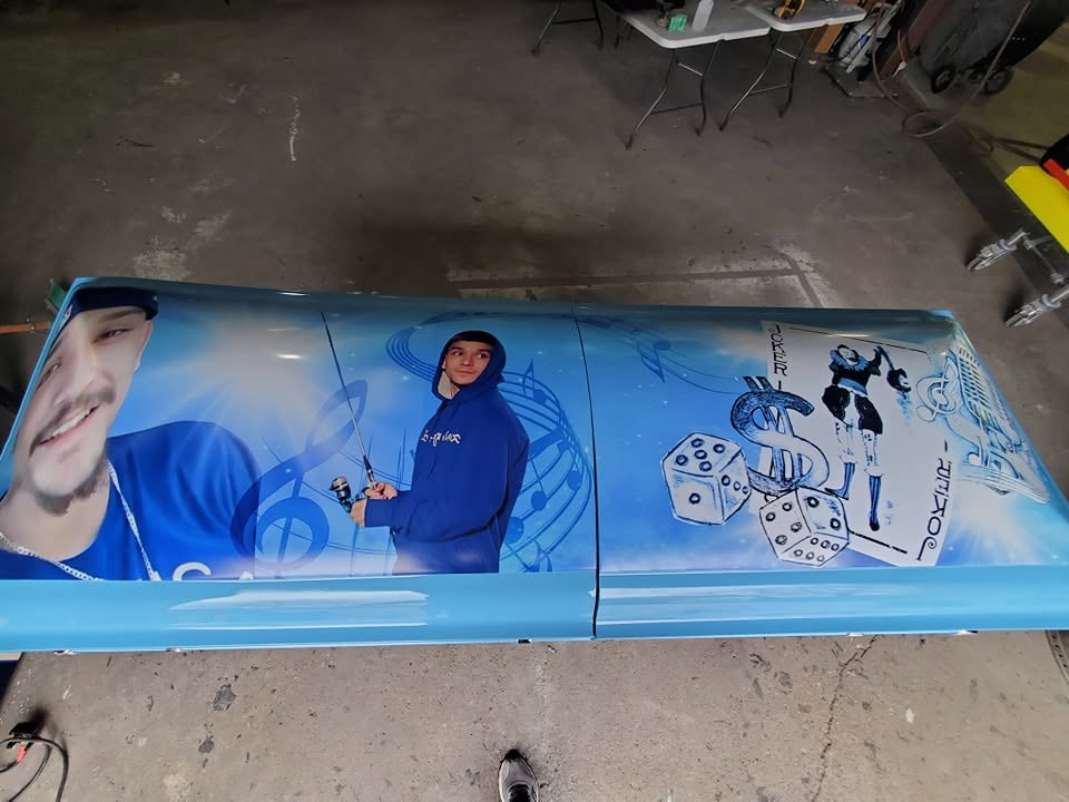 Sky blue casket lid wrapped with portraits, music notes, dice and a pair of joker cards