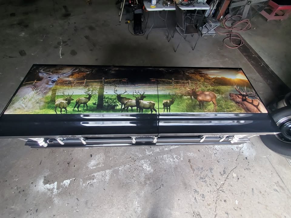 Black casket wrapped in a wildlife mural of bull elk and whitetail bucks in a green pasture