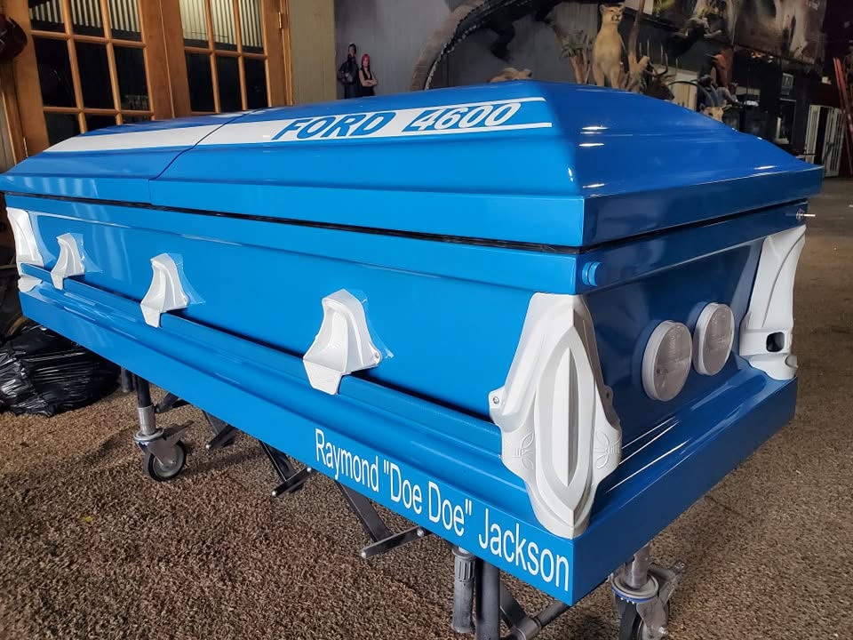 Tractor blue casket lettered FORD 4600 with white trim, named for Raymond Doe Doe Jackson