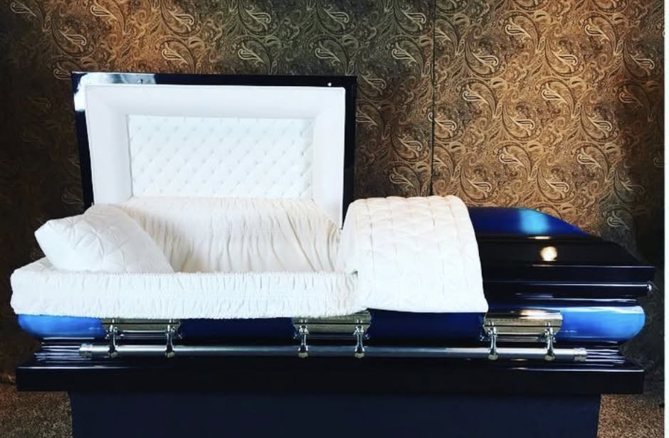 Two tone blue and black casket opened to reveal ivory crepe lining and a matching pillow