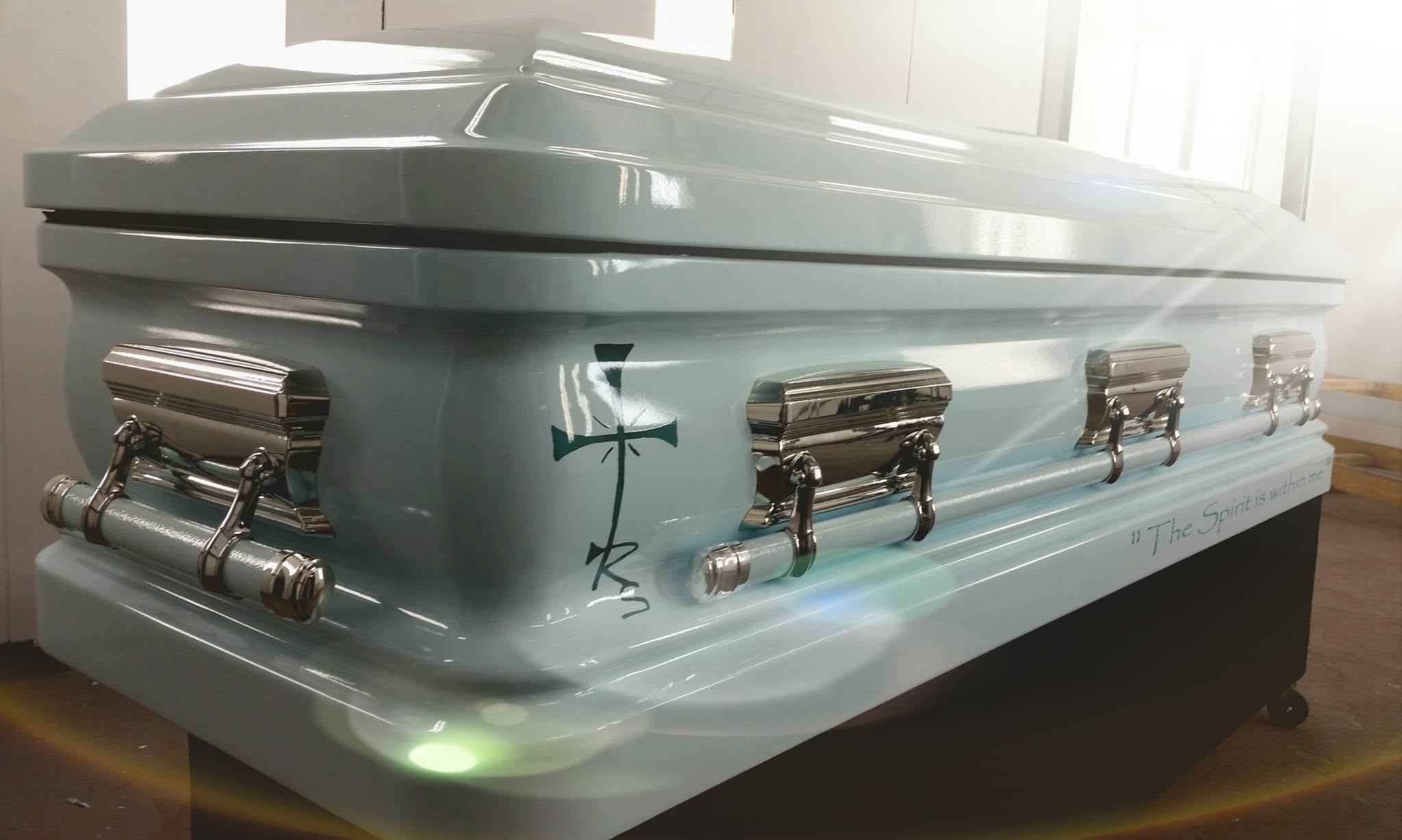 Powder blue high gloss casket with polished chrome handles, a slim cross and hand lettered scripture