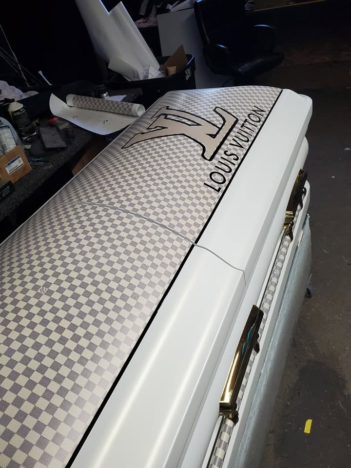 White casket wrapped in a gray checkerboard Louis Vuitton damier print with gold bar handles