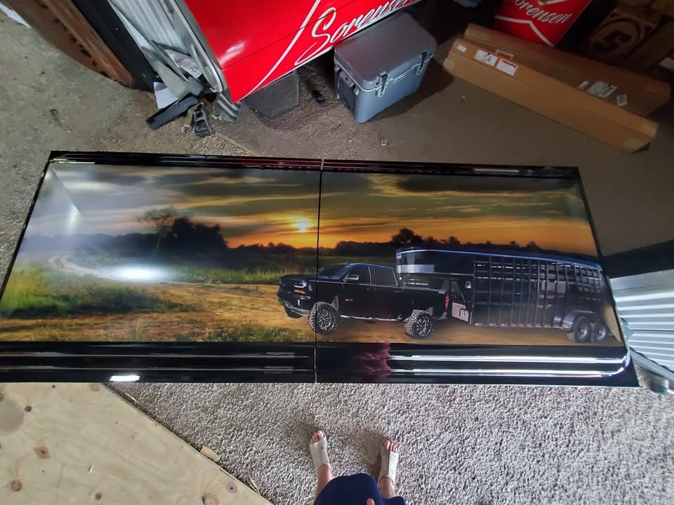 Black casket lid wrapped with a sunset pasture scene, black pickup truck and livestock trailer