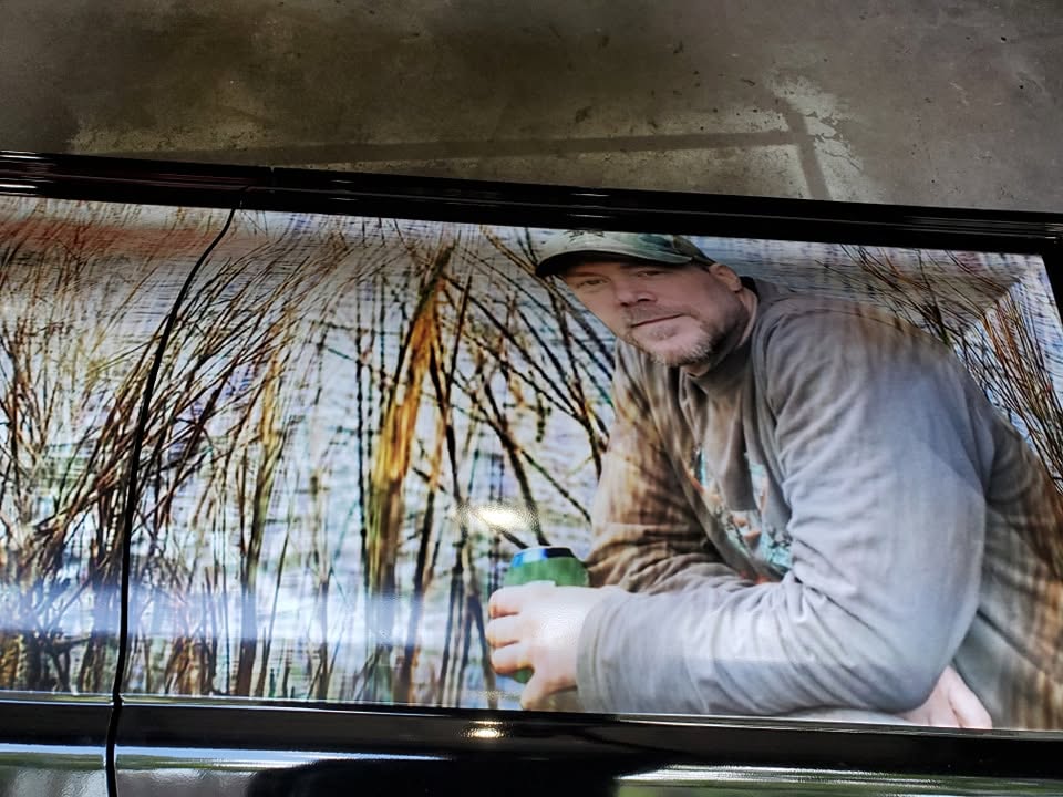 Glossy casket panel printed with a portrait of a man in a camo cap standing in winter brush