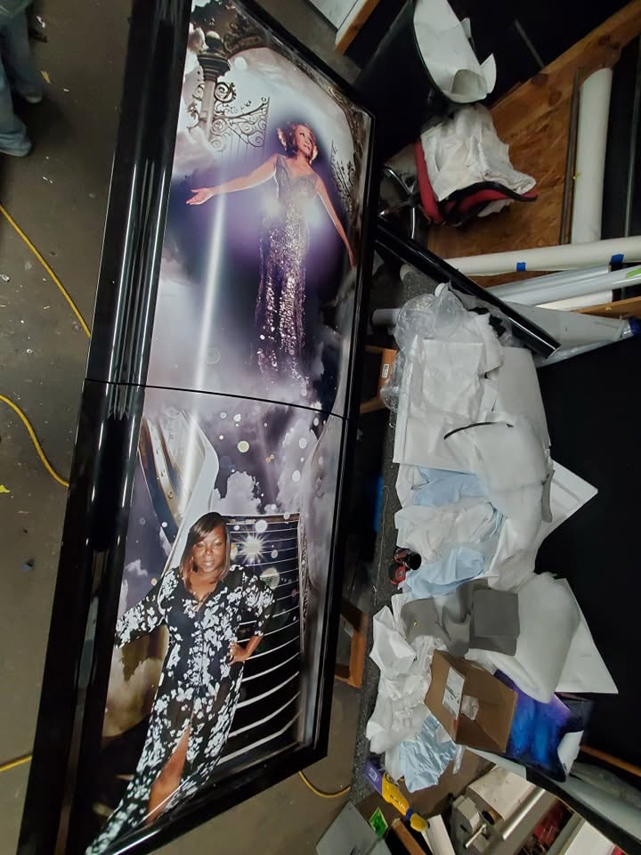 Black casket printed with heavenly cloud portraits of a woman in a sequined gown and floral dress
