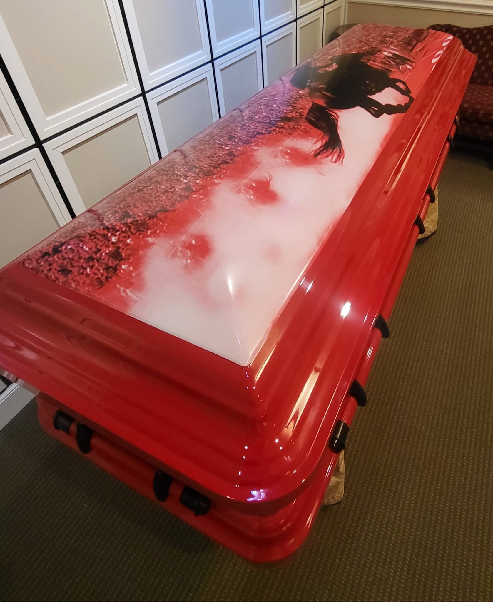 Candy red casket with a misty sunrise field and a buck deer silhouette on the wrap across the lid