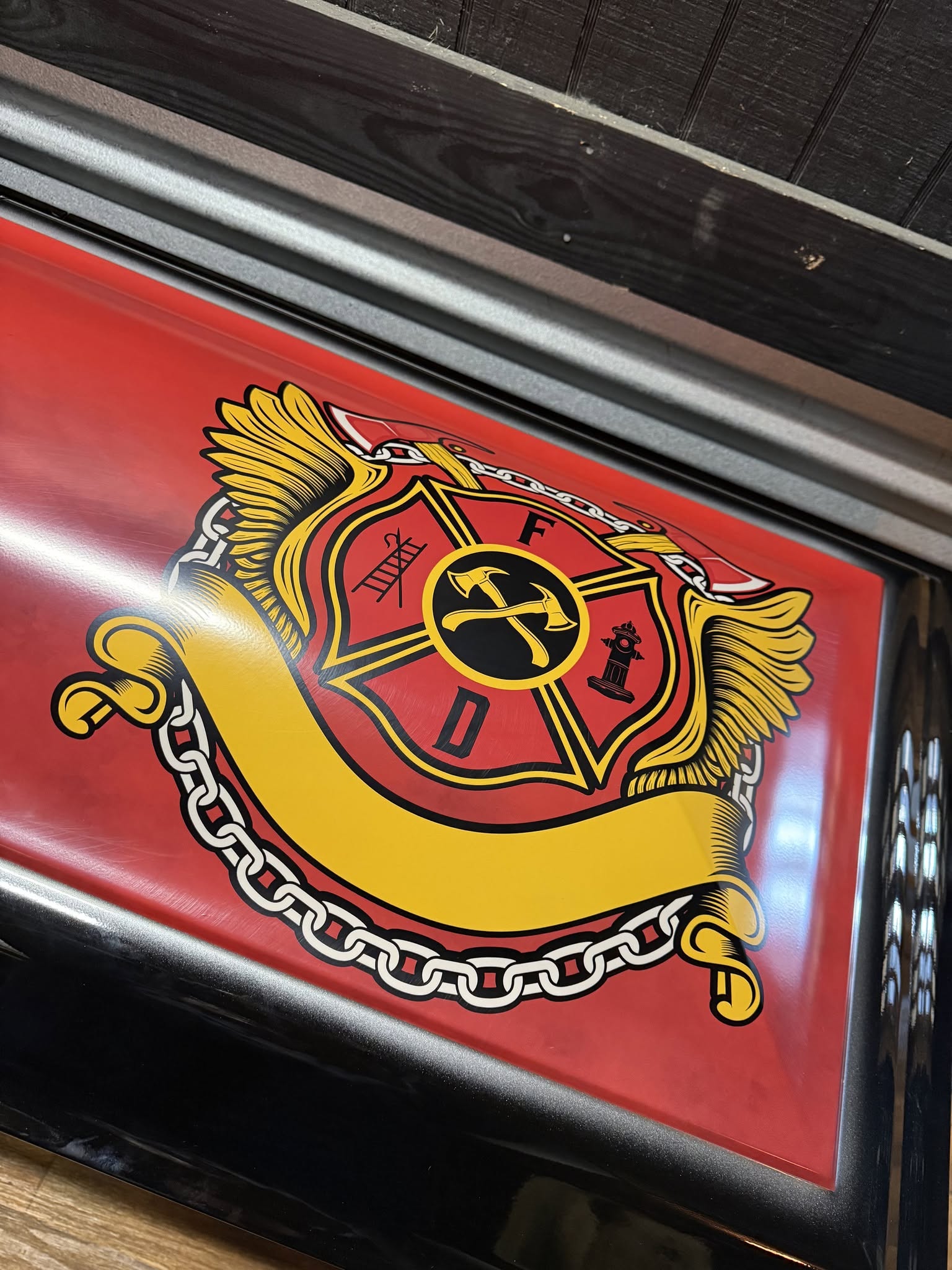 Red casket panel with a gold winged fire department Maltese cross, chain scroll and blank banner