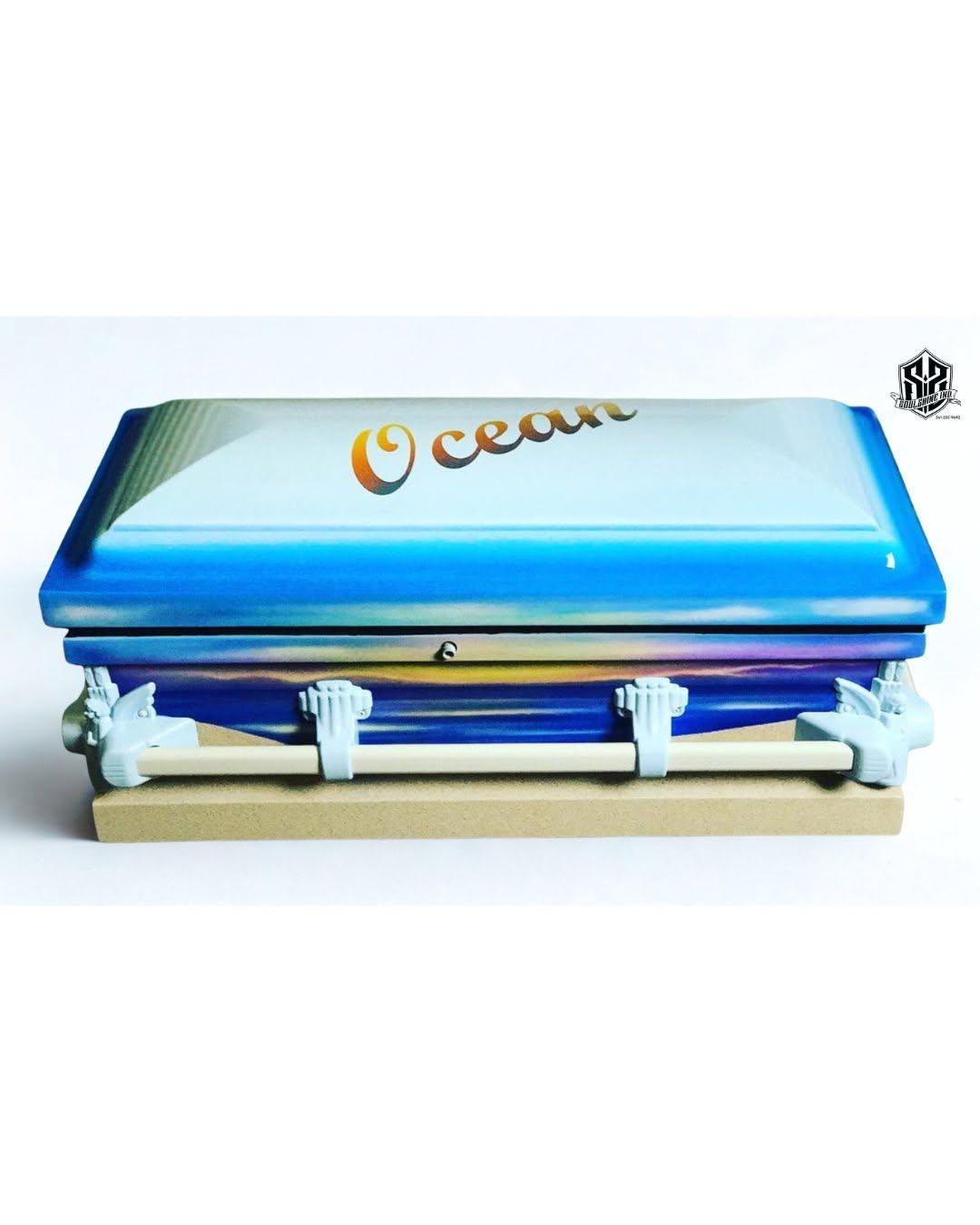 A wrapped ocean sunset design in blues with Ocean lettered on the lid of a small infant casket