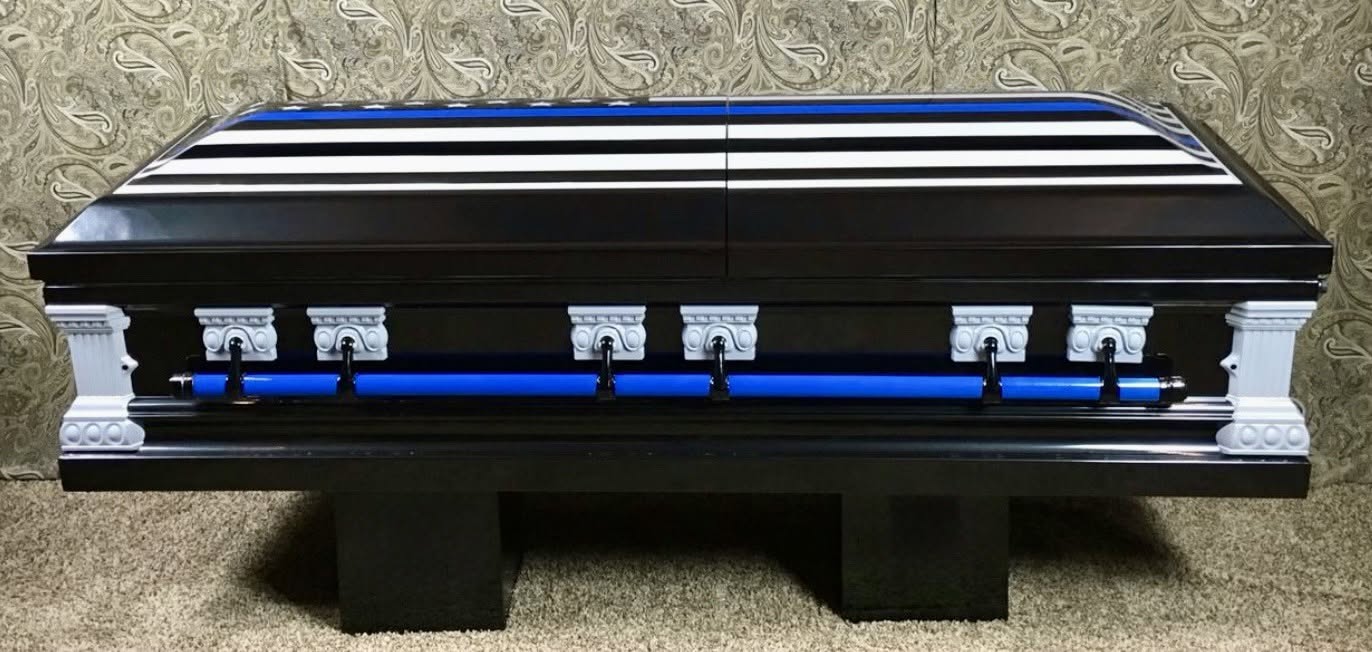 Thin blue line American flag across the lid of a black casket with white corner posts and blue bars