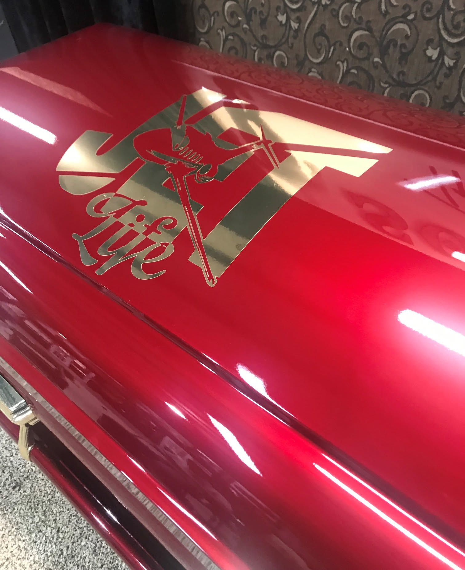 Candy apple red casket detailed with a gold Oilfield Life emblem and derrick artwork on the lid