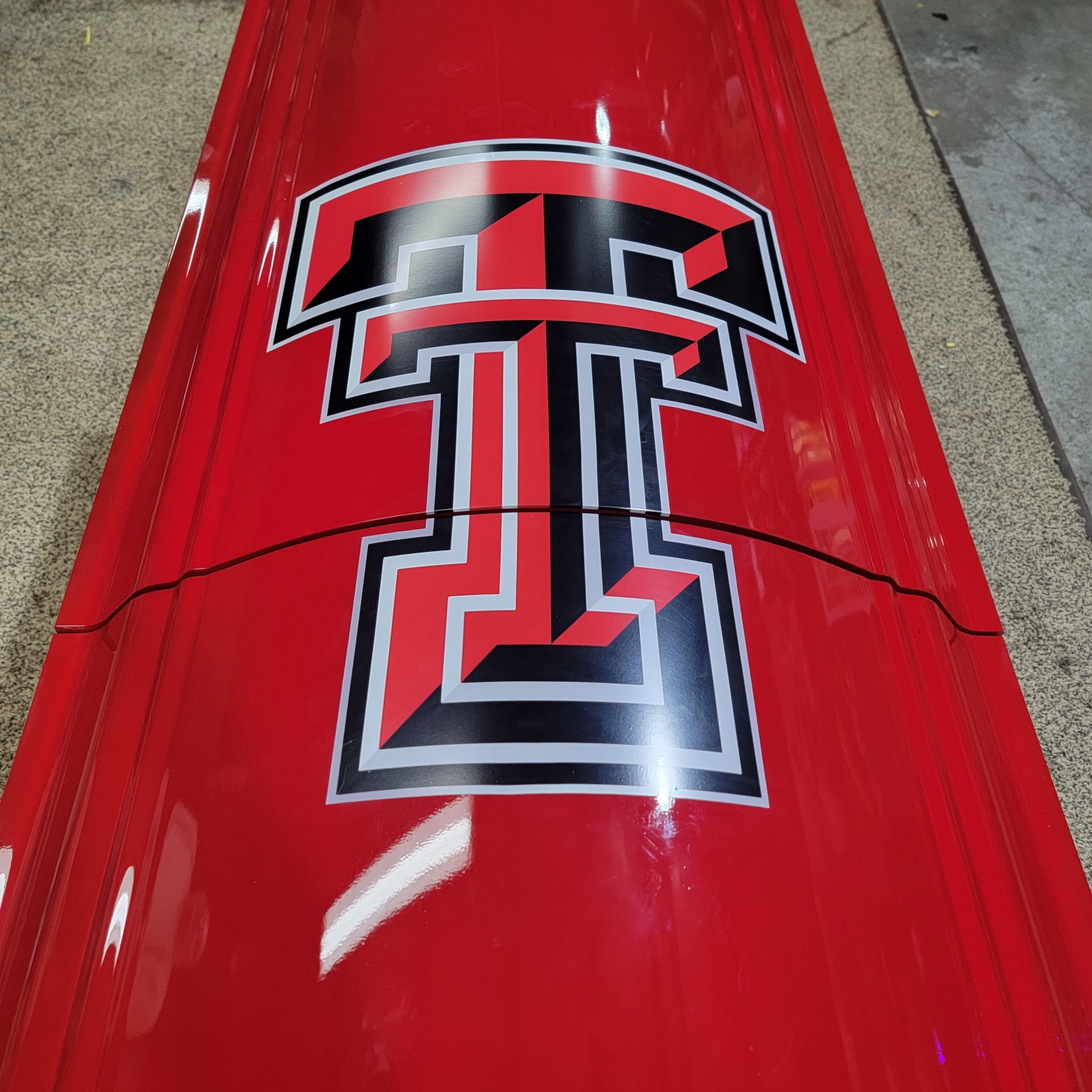 Close up of the black and white Texas Tech Double T decal centered on a gloss red casket lid