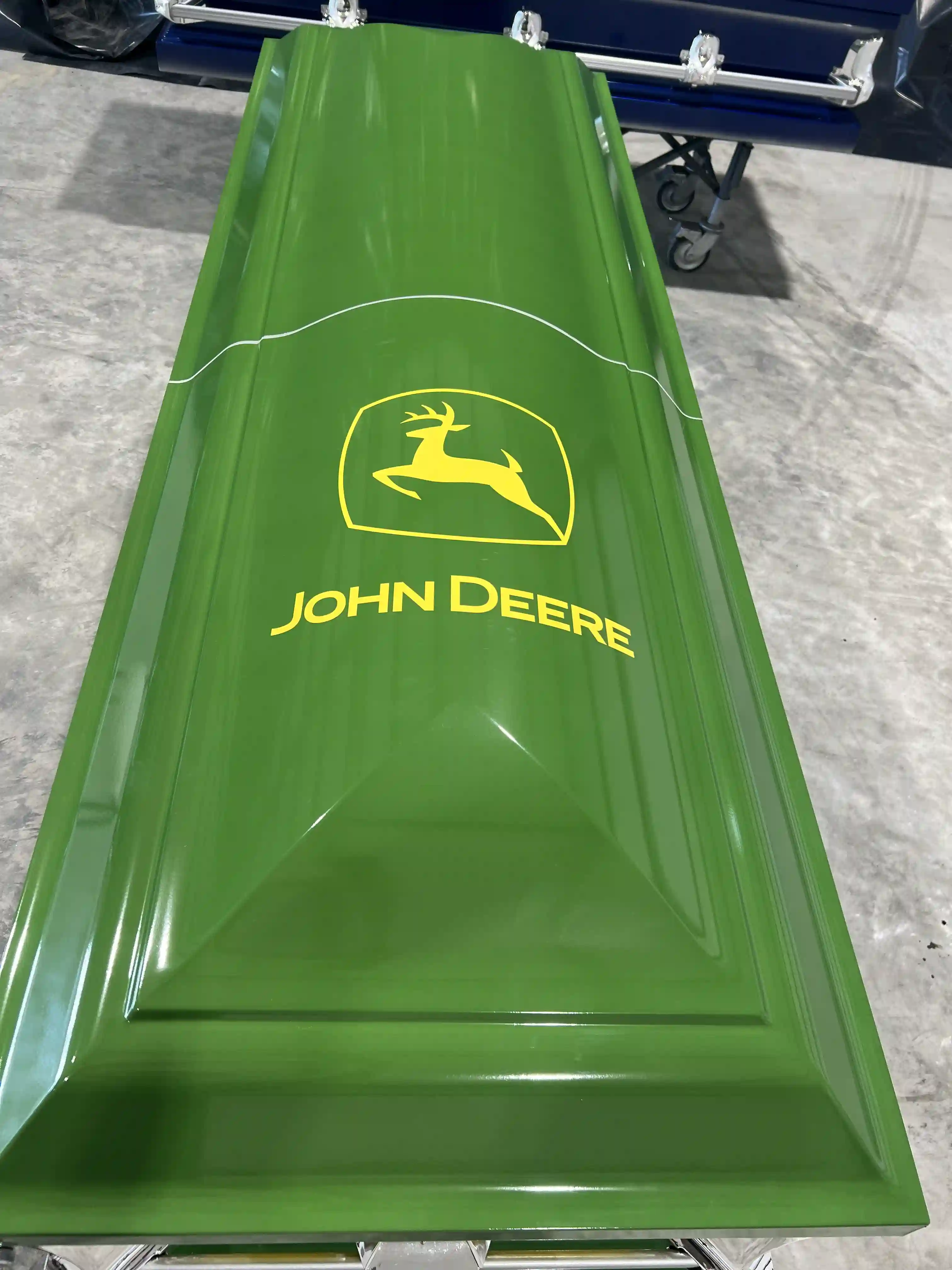 Top down look at the yellow John Deere leaping deer logo on the wrap of a bright green casket lid