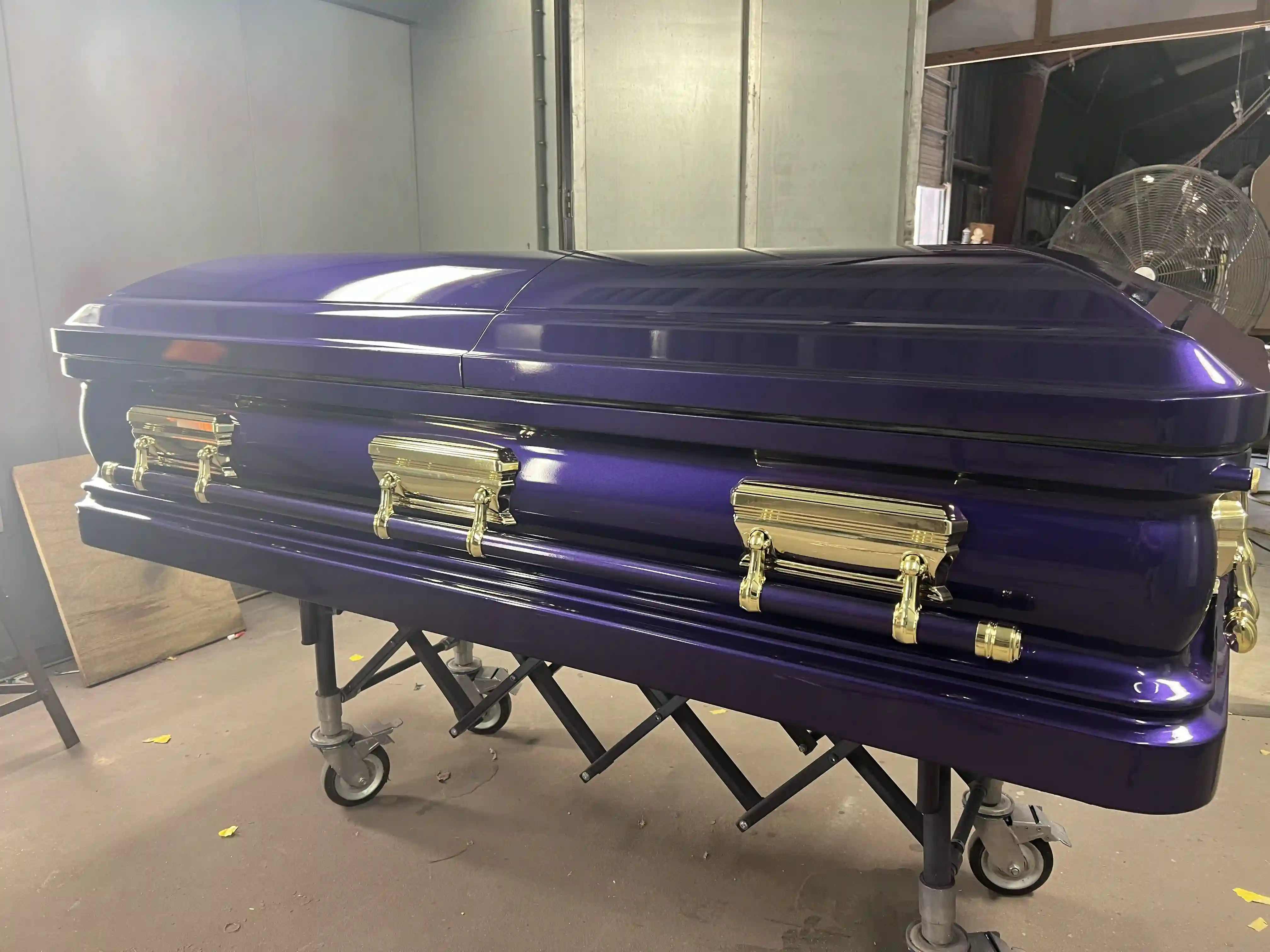 Deep metallic purple casket with polished gold bar handles rolled out on a church truck