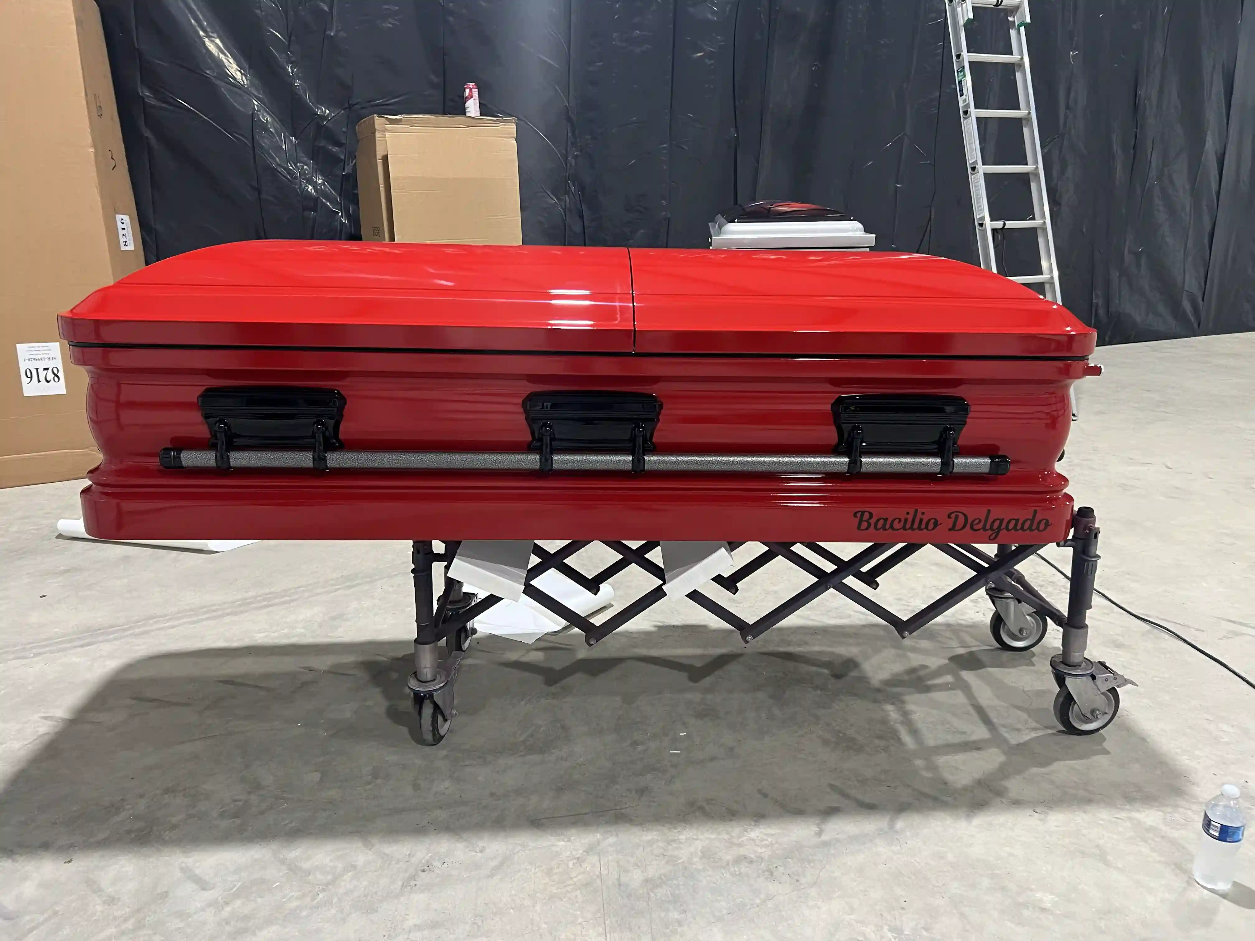 Gloss red casket with matte black bar handles and Bacilio Delgado lettered along the base
