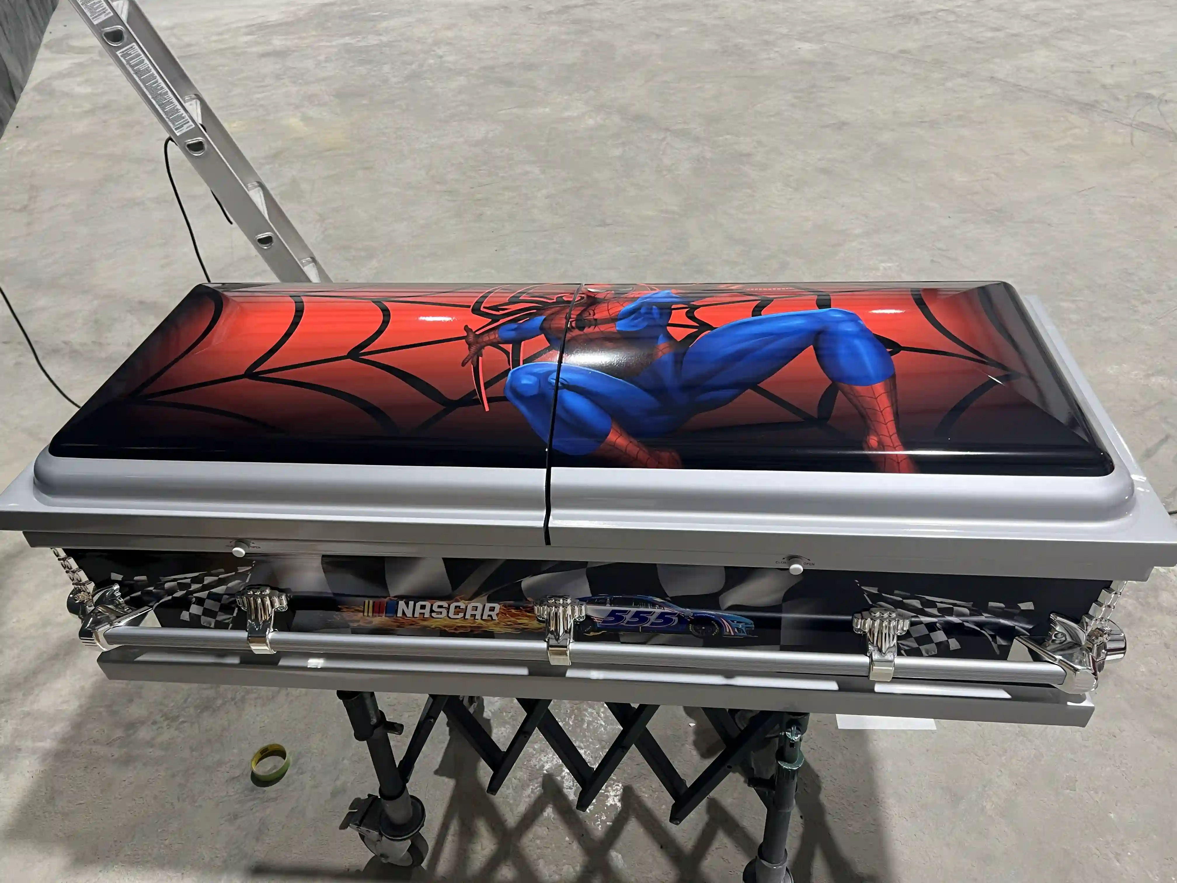 Spider-Man crawling across a red web on the glossy lid of a silver and black child casket