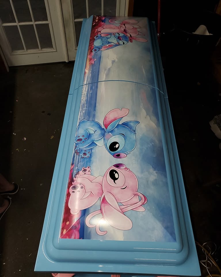 Light blue child casket wrapped with Stitch and Angel drifting through a cloudy sky