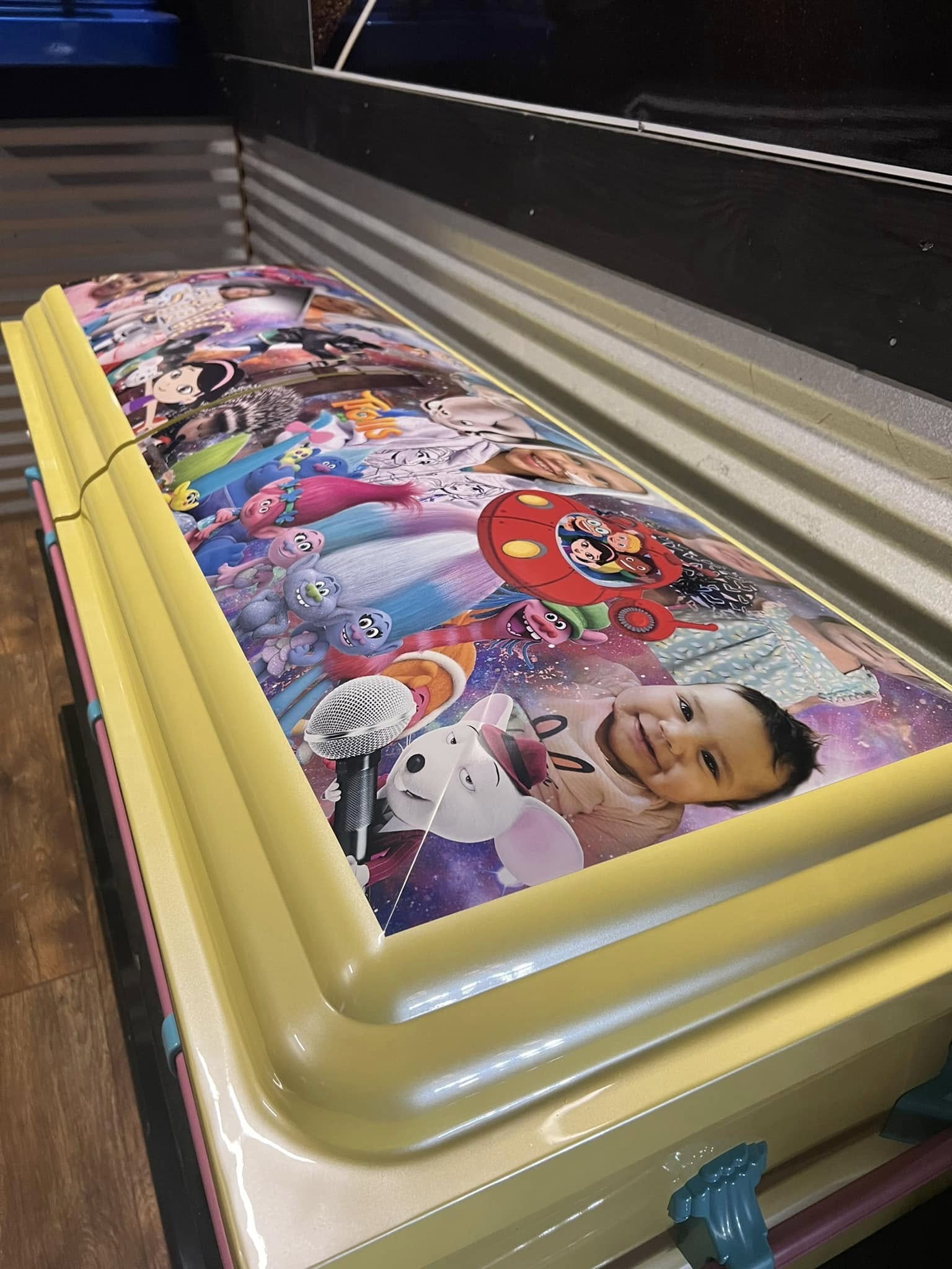 Pale yellow child casket with a Trolls and Cocomelon collage and a smiling toddler portrait