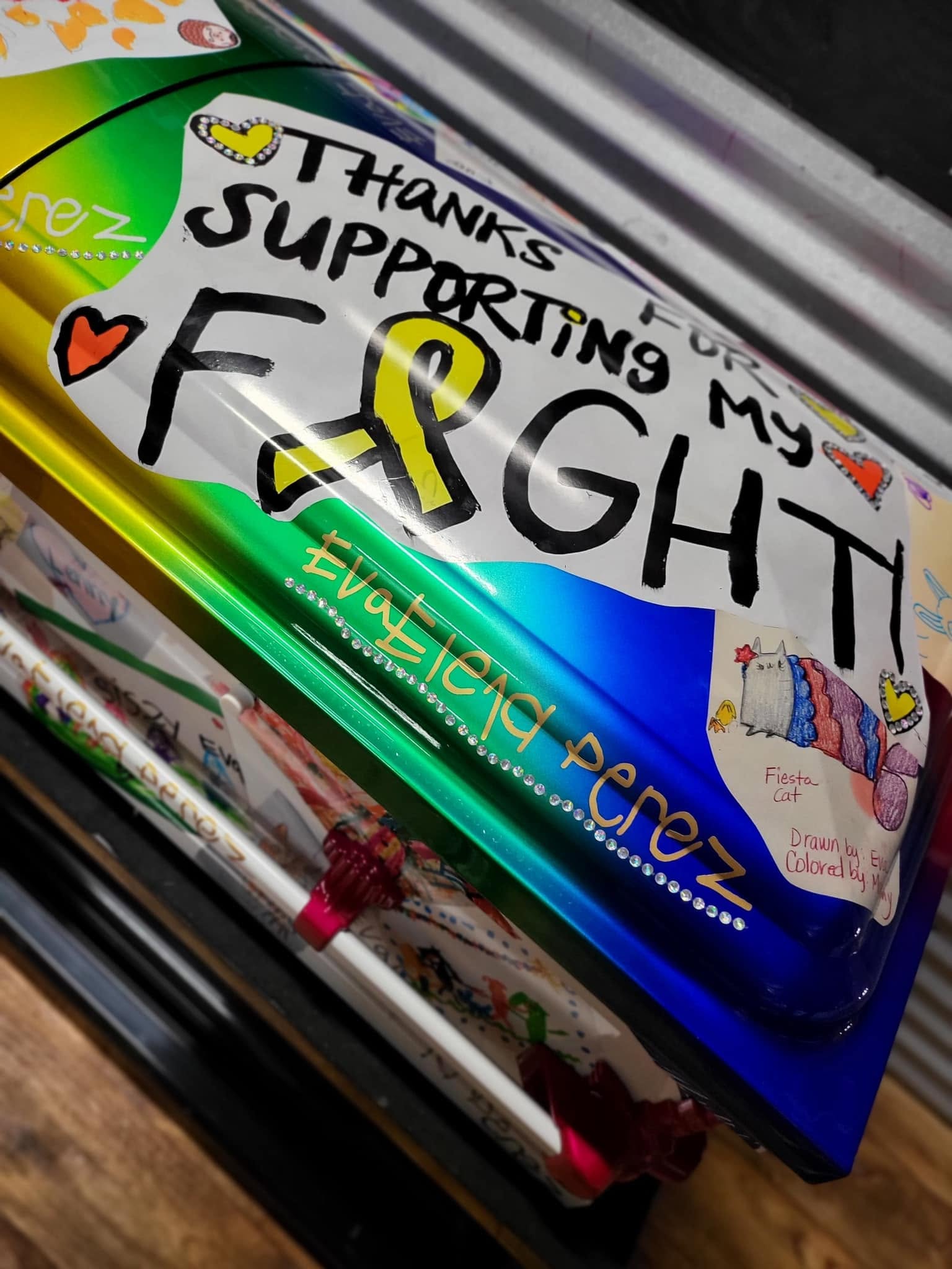 Rainbow wrapped child casket lettered Eva Elena Perez with hand drawn cards and a gold ribbon