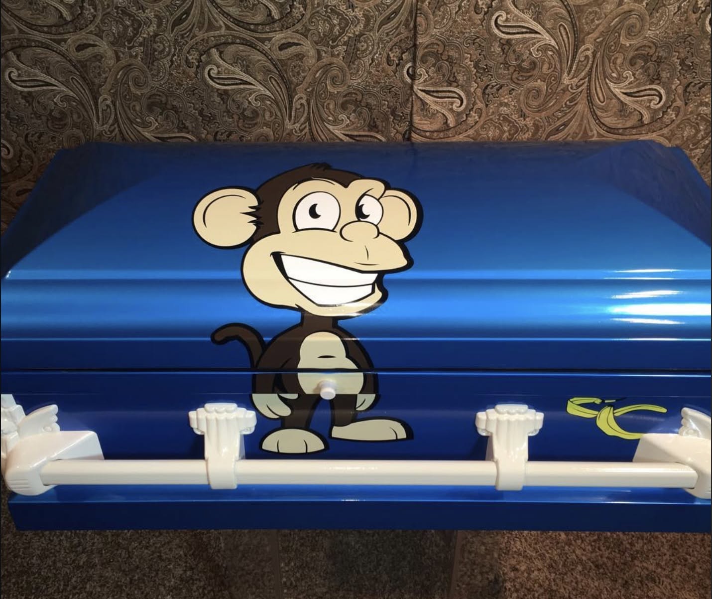 Glossy blue child casket with a cartoon monkey decal, banana detail and white bar handles