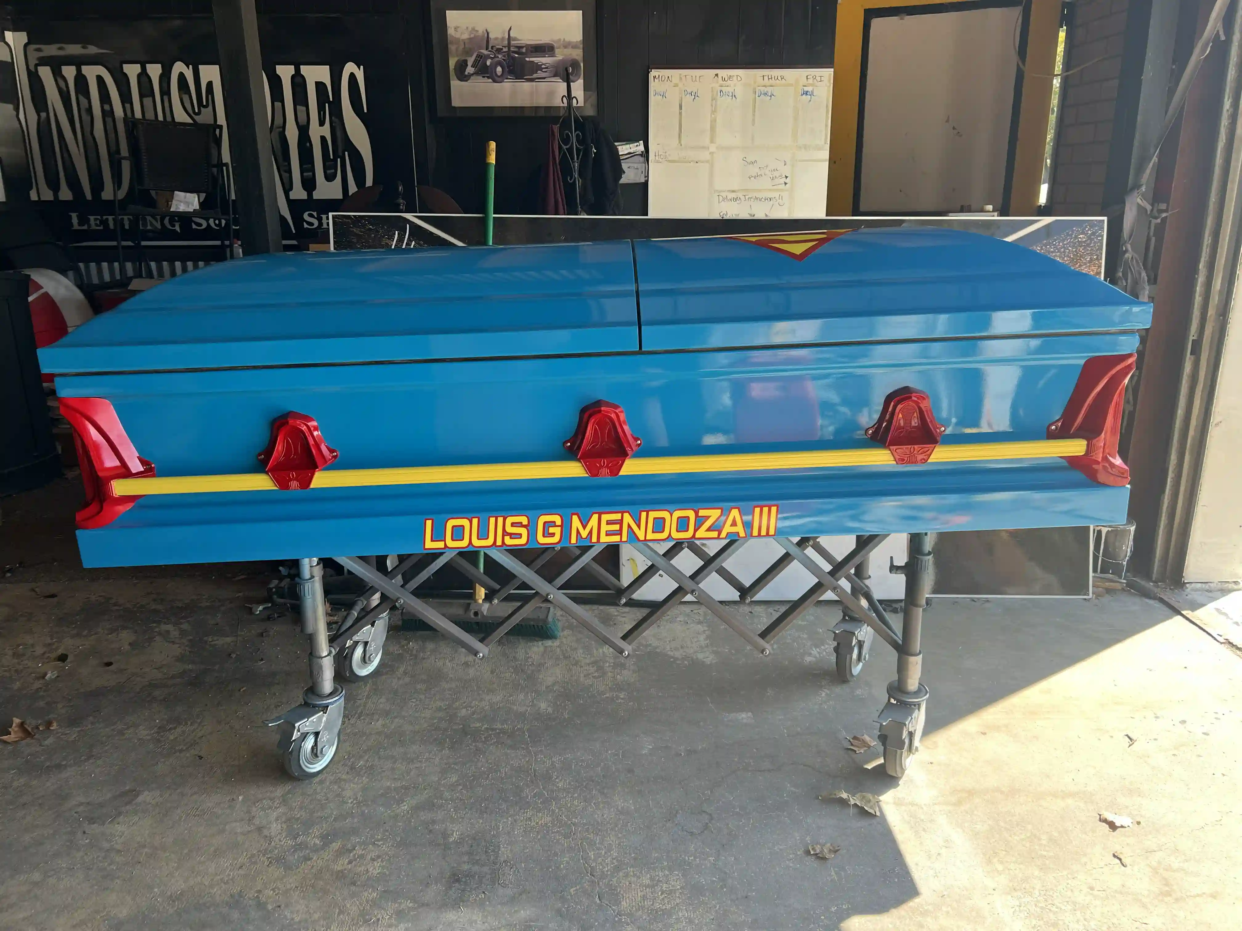 Superman blue child casket with red handles and a yellow stripe lettered Louis G Mendoza III