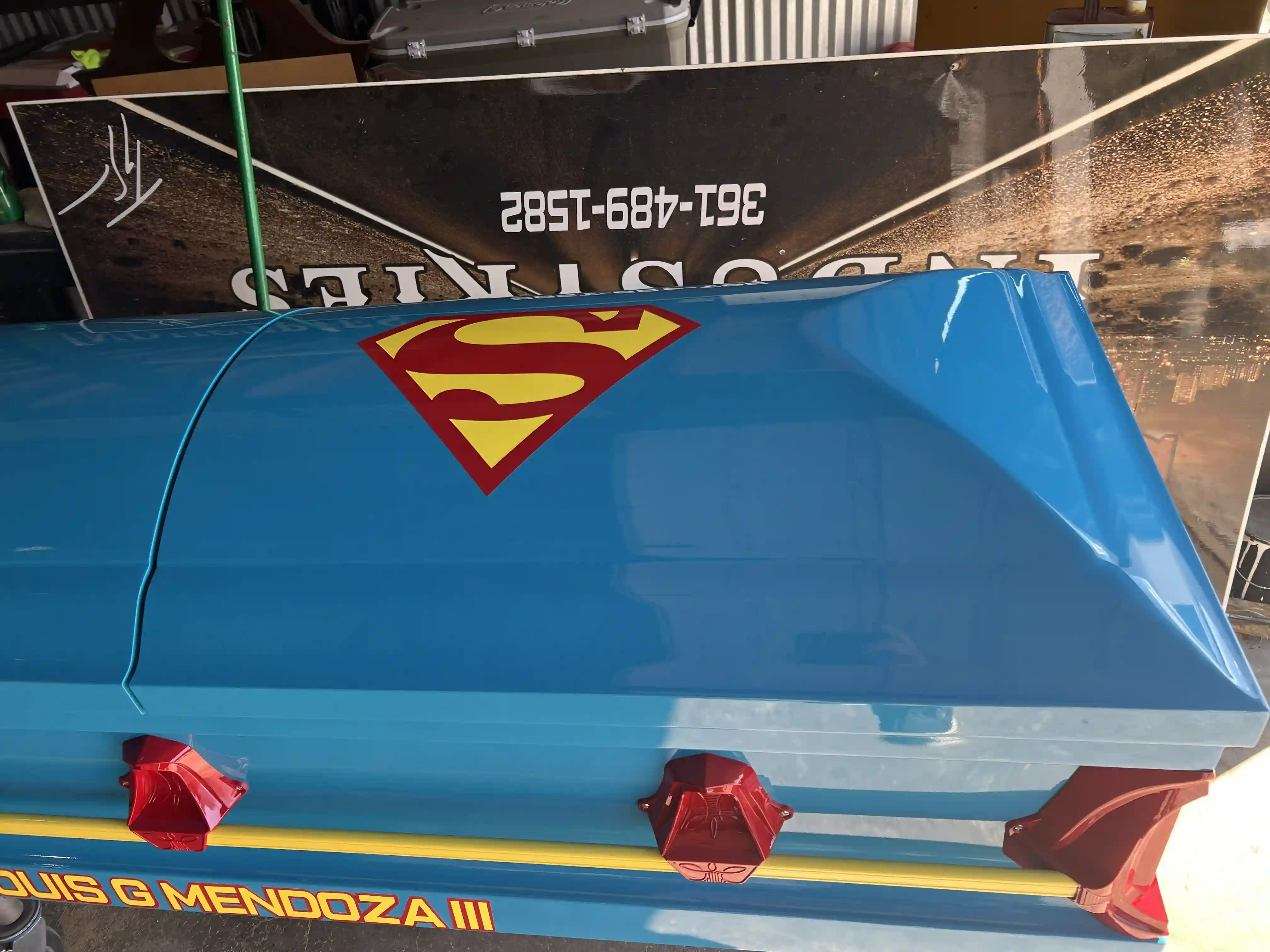 Superman shield decal on the sky blue lid of a child casket with red handles below
